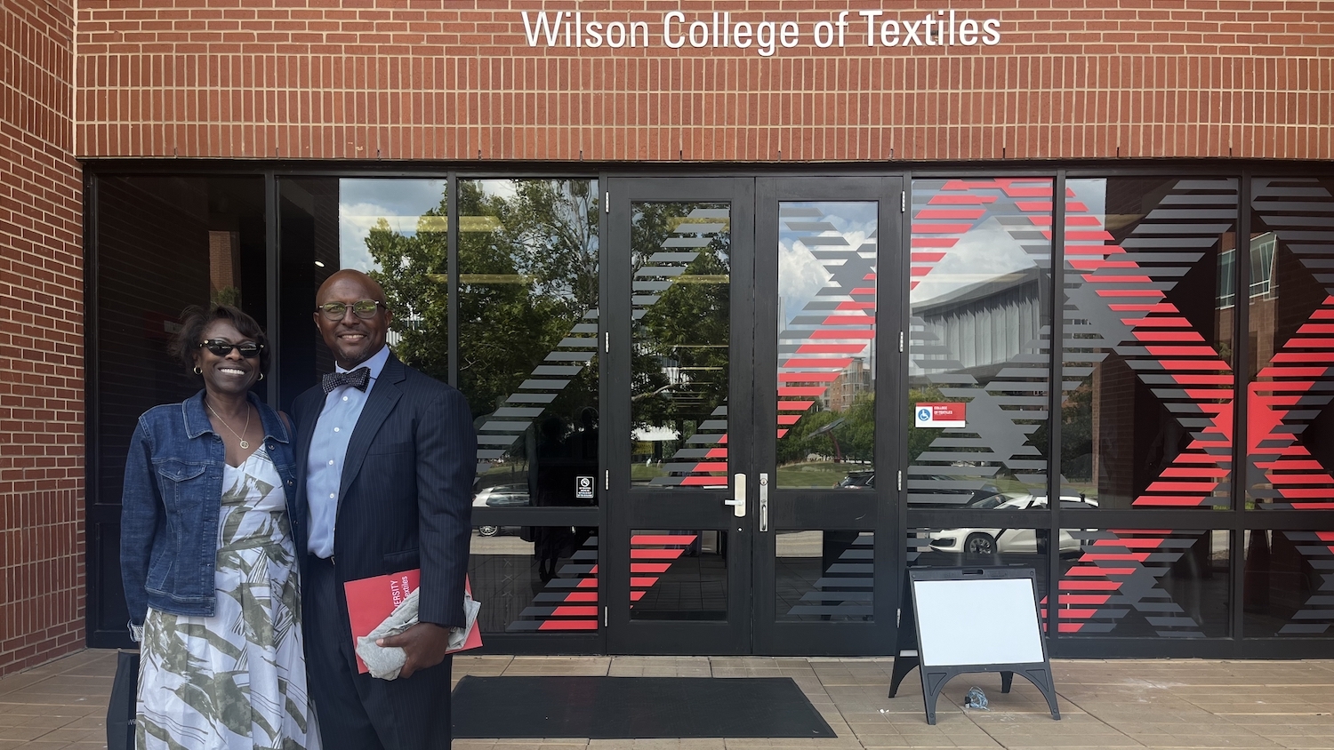 Shannon and John Peterson standing in the bottom-left corner of the photo, with a Wilson College of Textiles building behind them.